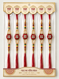 Six Rakhi thread bundles packaged in a clear plastic sleeve with a decorative cream and red cardboard backing.