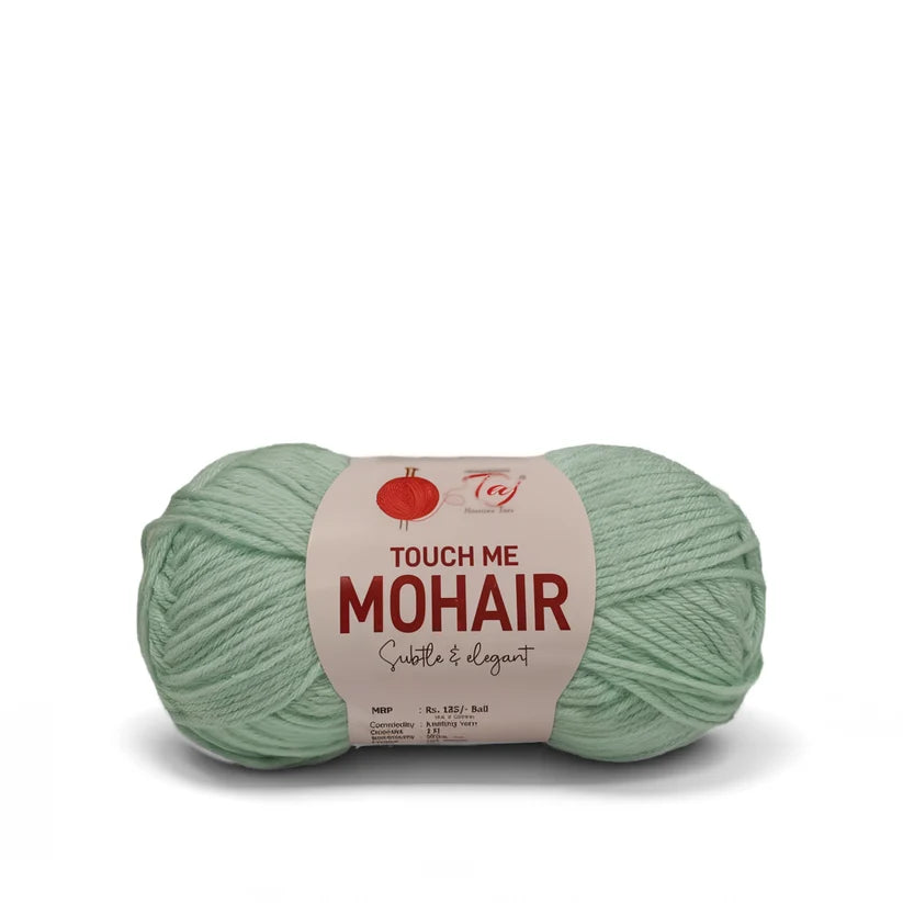 A ball of sage green mohair yarn with a paper label that reads 'TOUCH ME MOHAIR'