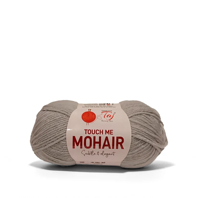 A skein of Taj Touch Me Mohair yarn in a soft taupe-beige color, wrapped with a paper label