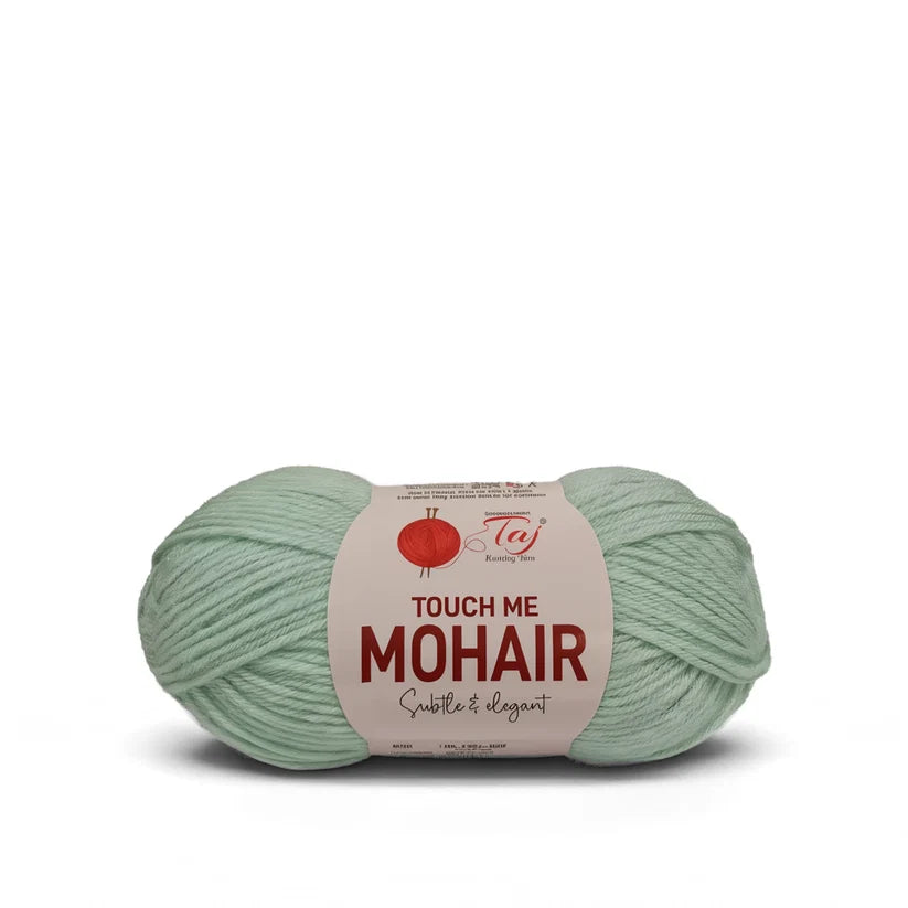 A skein of sage green mohair yarn with a paper label that reads 'TOUCH ME MOHAIR'